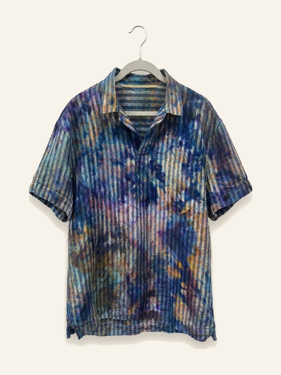 Hand ice-dyed linen short-sleeve polo in indigo, violet, and amber stripes on a pale grey hanger